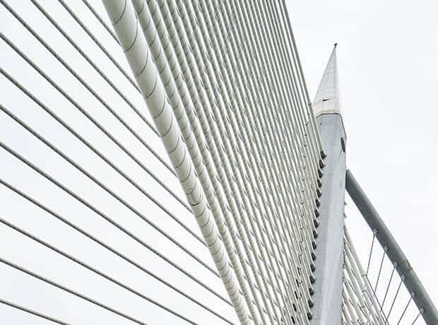 Close-up view of white suspension cables and support tower of a modern cable-stayed bridge against a light sky.