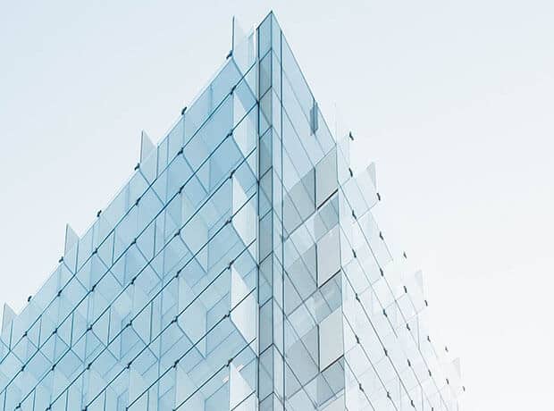 Modern glass building with angular geometric facade panels, photographed against a clear, pale sky.